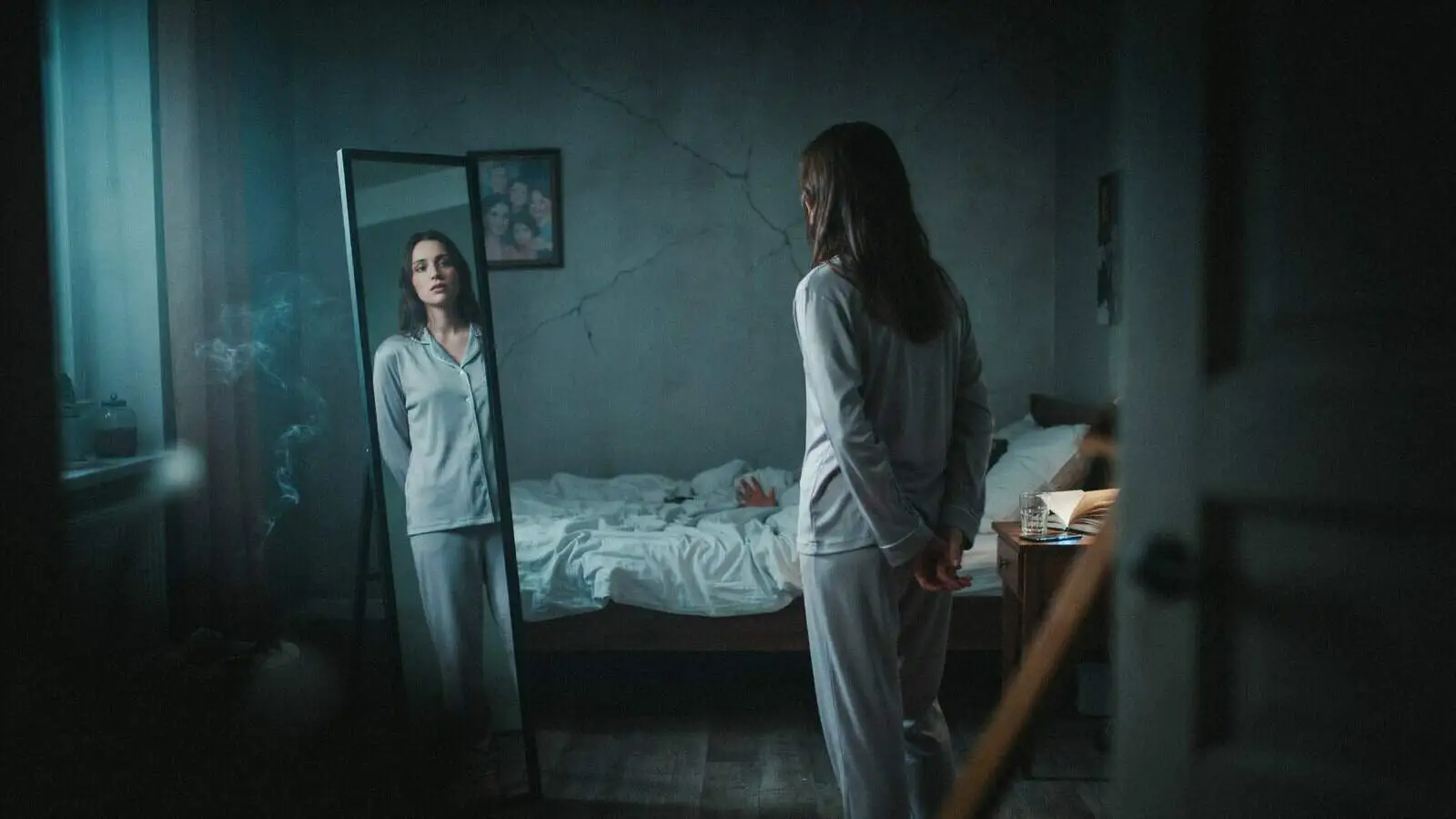 Woman facing her reflection in a dark bedroom representing psychological thriller movies