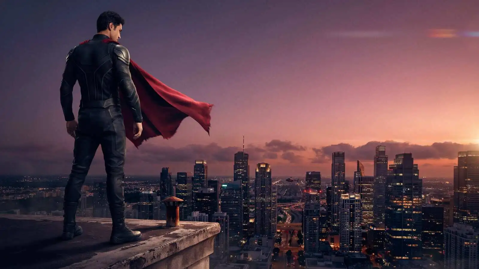 Original caped superhero overlooking a city skyline at sunset
